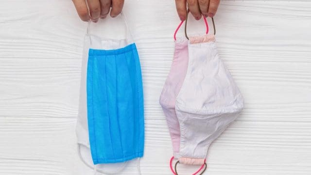Hands holding reusable face masks and single use medical masks on white wooden background. Zero waste lifestyle during virus outbreak. Disposable mask and handmade textile mask