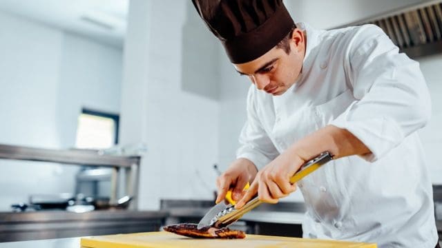 Cropped shot of a young male chef cutting the meat in a professional kitchen
