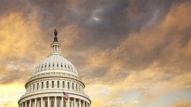 The dome of the United States capitol with an American flag and dramatic clouds behind