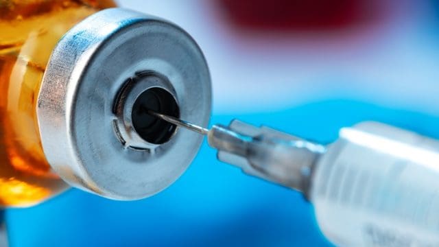 Vaccine bottle with a syringe taking the vaccine from it close up.
