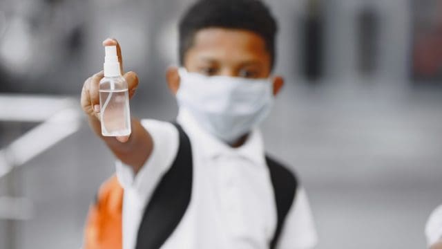 African boy holds antiseptick. Child in a summer city. Coronavirus theme.