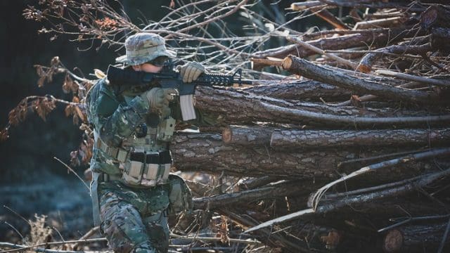 Airsoft military game player in camouflage uniform with armed assault rifle.