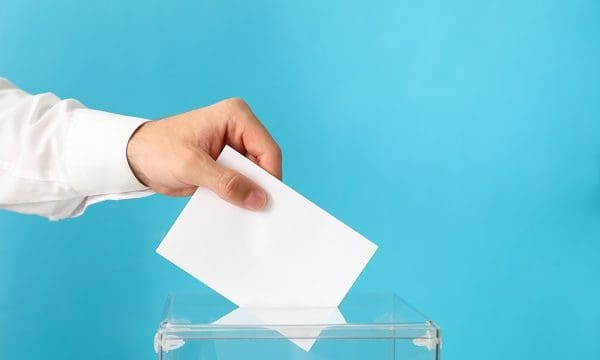 Man putting ballot into voting box on blue background