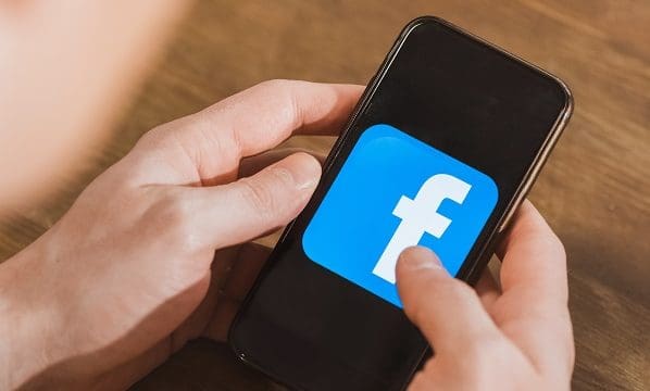 Man using smartphone with facebook logo icon on screen