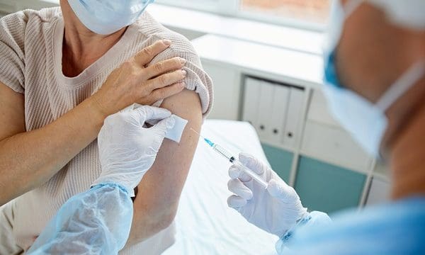 Modern medical worker giving injection with vaccine to unrecognizable female patient into shoulder, high angle view shot
