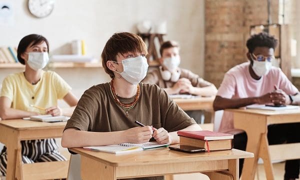 Group of students in protective masks sitting at desks and studying at school