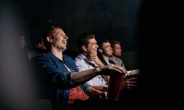 Group of friends sitting in multiplex movie theater. Young people watching movie in cinema hall and smiling.