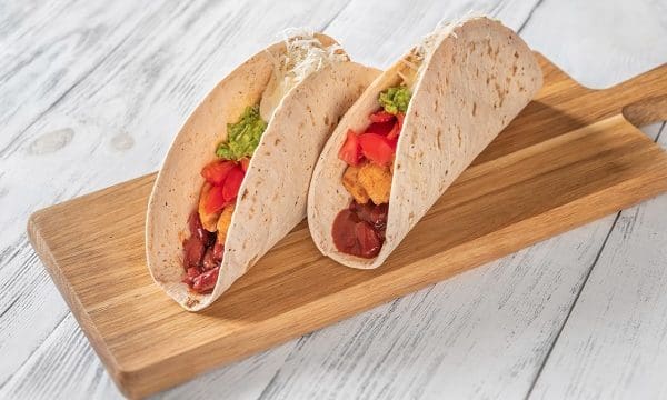 Taco with chicken and vegetable filling on the wooden background