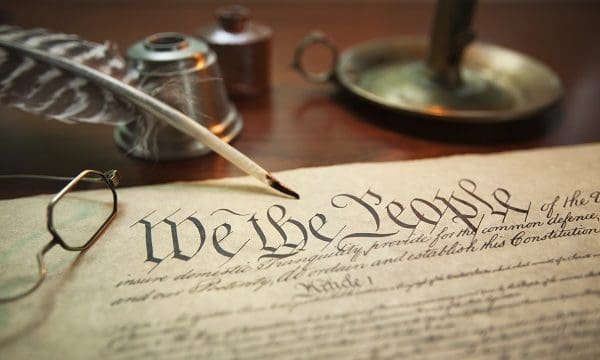 Selective focus image of the United States Constitution with quill pen, glasses and candle holder