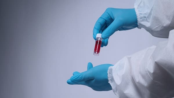 Blood tests in clear tube on doctor hands with blue medical gloves and PPE suit which represent coronavirus or 2019-ncov or covid-19 pandemic screening test that positive results or infected