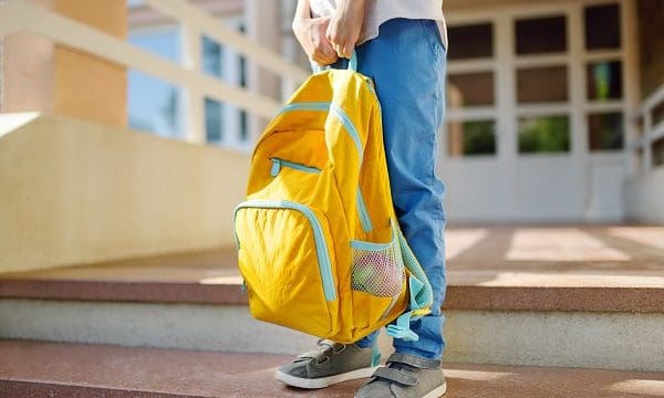 Little student with a backpack on the steps of the stairs of school building. Close-up of child legs, hands and schoolbag of boy standing on staircase of schoolhouse. Kids back to school concept.