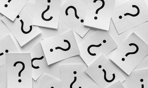 Background texture of printed question marks on white sheets of paper scattered randomly overlapping in a full frame view