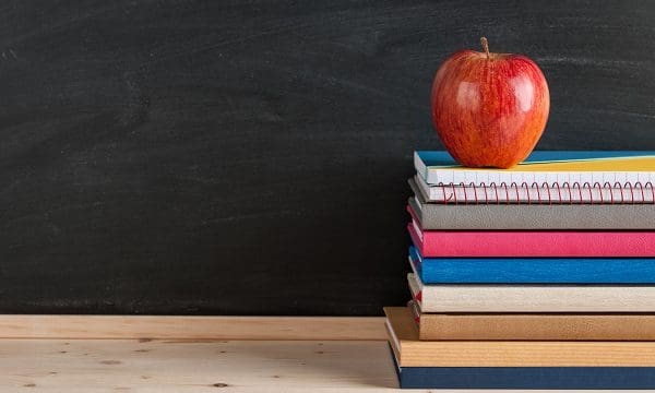 Red apple top a stack of books and notebooks on blackboard background