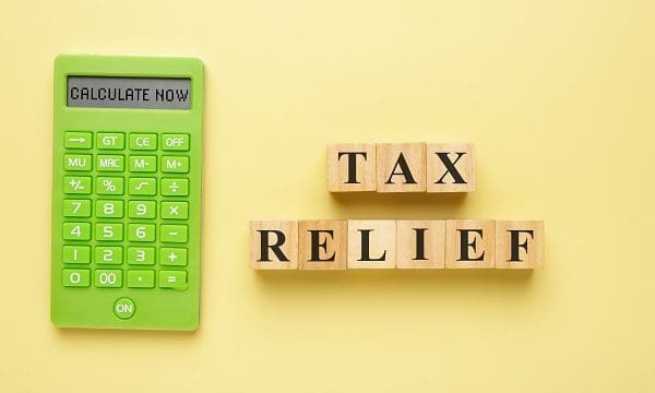 Flatlay picture of wooden block written Tax Relief with calculator and calculate now word.