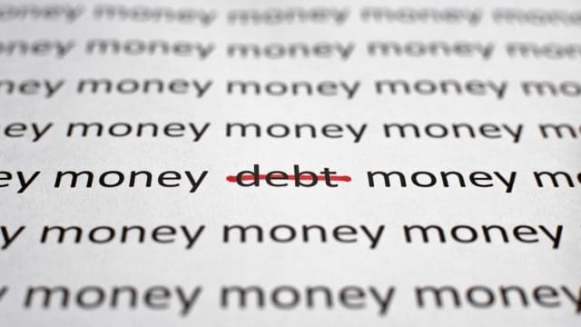 Printed text Money and Debt on white paper, close-up. Financial problems, economics and business concept. Selective focus on word debt crossed out with red line, low angle view, macro photo.