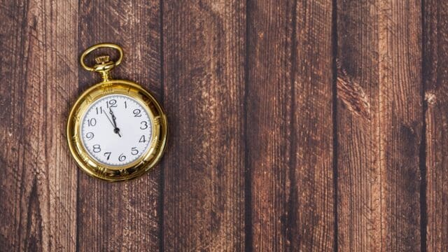 Vintage golden clock showing midnight, on wooden background