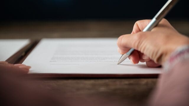 Low angle view of female hand signing document, contract or application form with a pen.