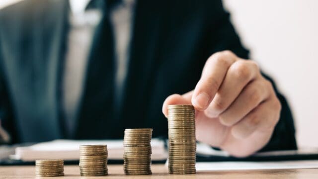 Asian investors man are placing coins in a growing position with savings finance money concept.
