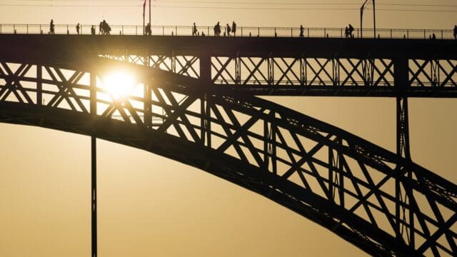 Silhouette of bridge construction with people walking against bright golden sunlight in evening