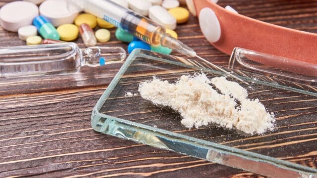 Drugs overdose leads to death. White powder on glass. Syringe, pills, wooden background.